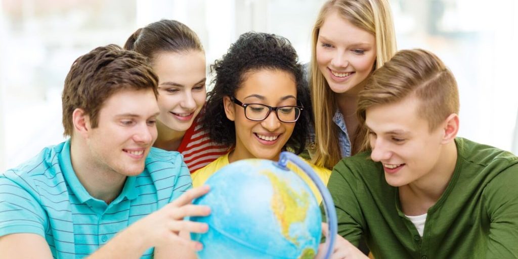 five smiling students looking at earth globe