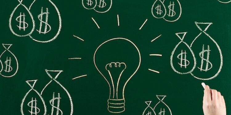 hand drawing a lightbulb and bags of money on a chalk board